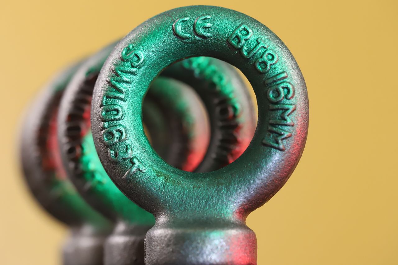 Round metal forged eye bolts used for lifting heavy applications arranged in row on yellow blurred background in light studio